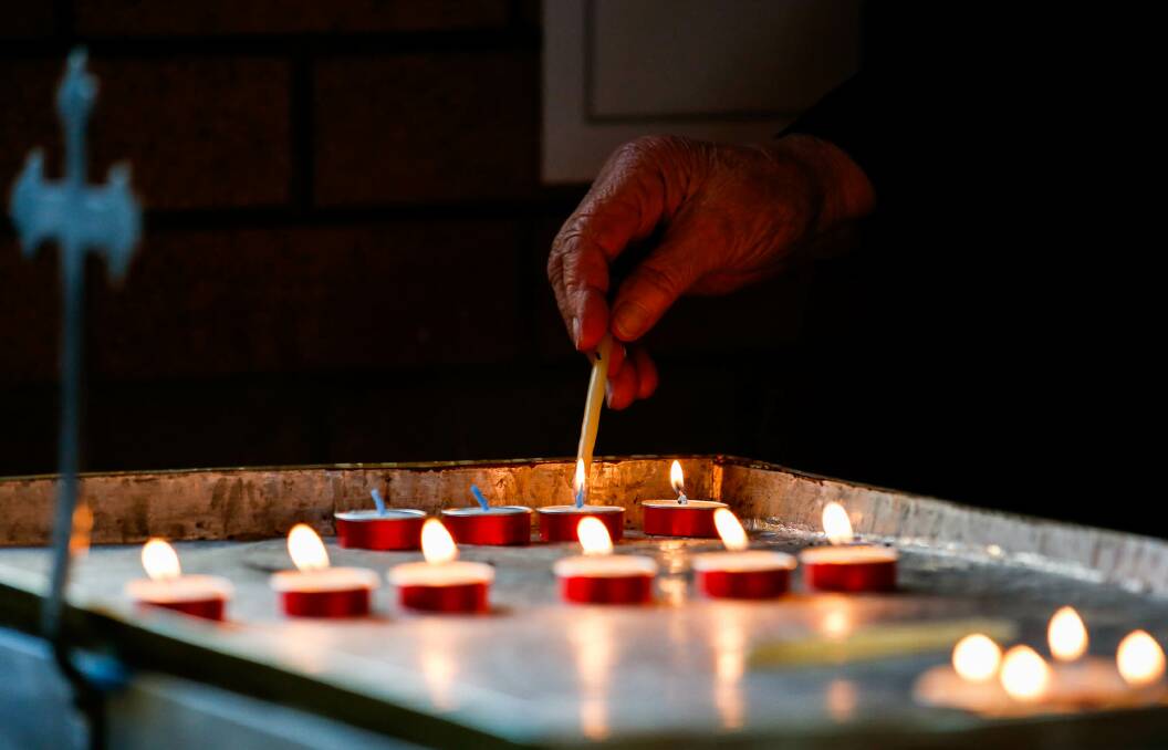 Father Simon Ckuj conducts a prayer service for Ukraine at St Volodymyr Church in Wollongong, with many Ukrainian expats in attendance. Markusia Boger lights a candle and prays for Ukraine. Picture: Anna Warr