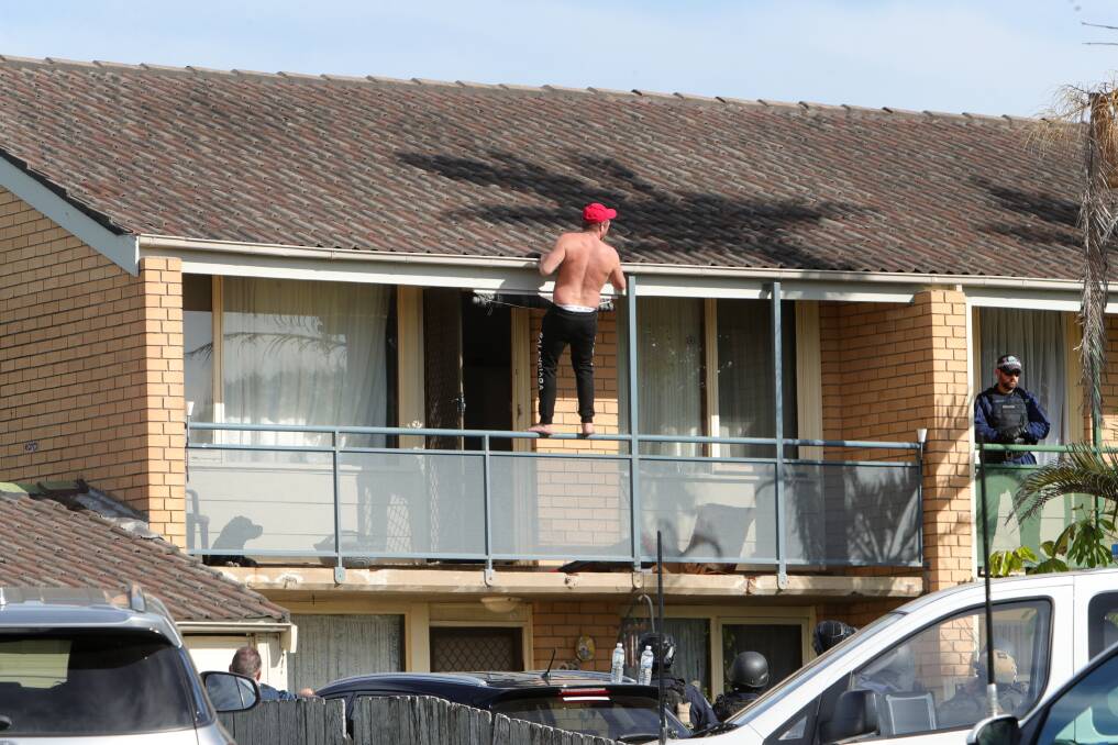 The man climbs onto a balcony railing as the standoff enters its third hour. Pictures: Sylvia Liber 