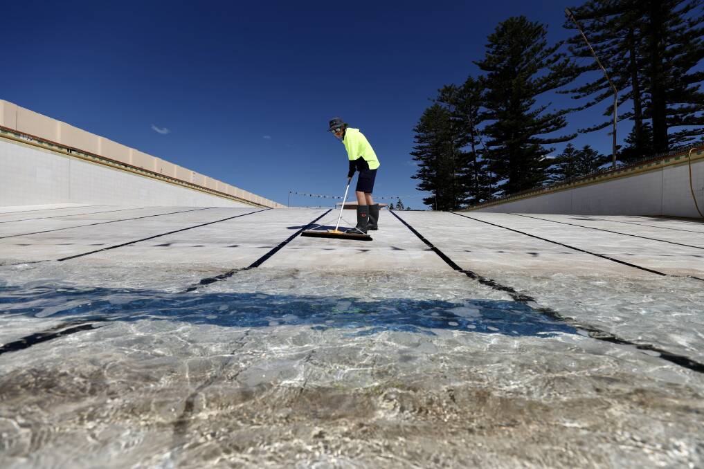 Council lifeguard Jacob McMaster gets to work on Thirroul Pool ahead of its opening this weekend. Photo: Adam McLean 