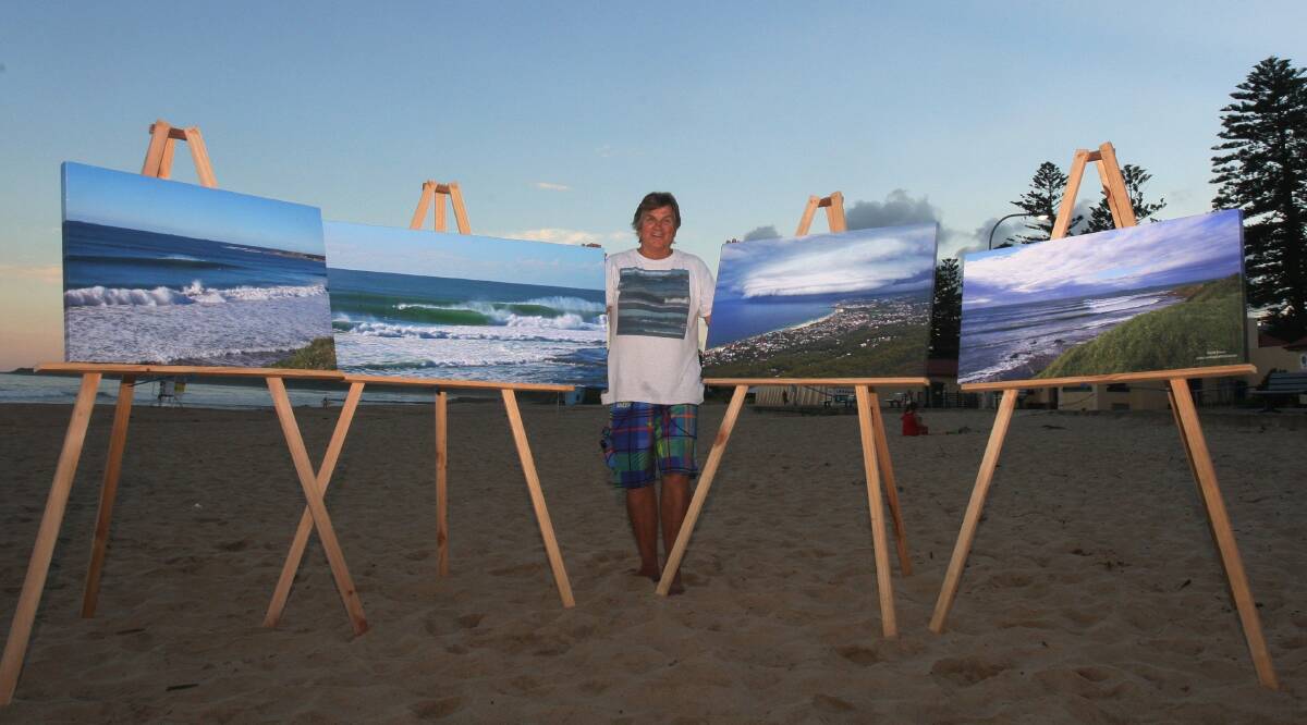 Surf photographer Clarrie Bouma with some of his work on Thirroul beach. A paddle out in his memory will take place on Saturday. Picture: Robert Peet
