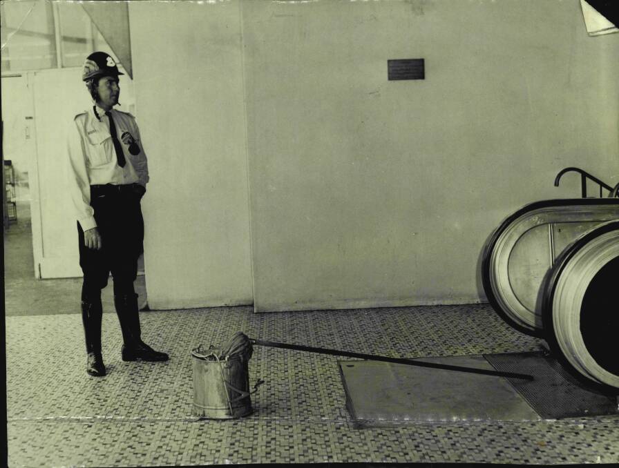 A policeman stands near Wilhelmina Kruger's mop and bucket at Piccadilly, where it was left after an unknown assailant dragged her down the escalator and into the car park before murdering her.