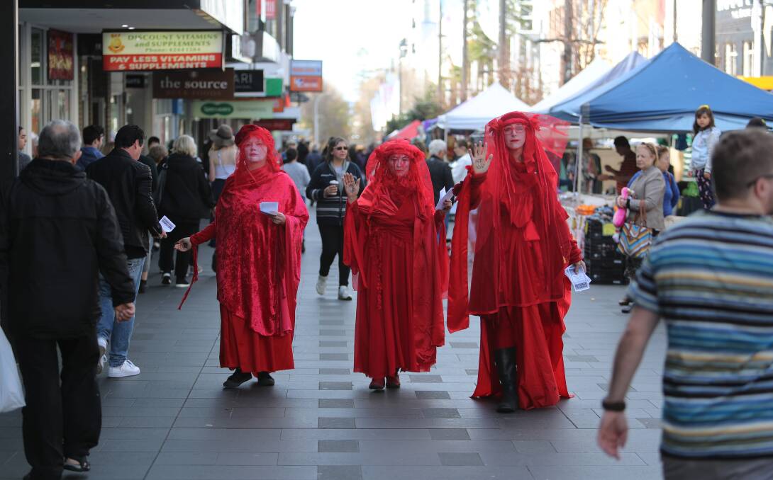 The women in red pulled back their veils with dozens pretending to 'drop dead' during an environmental protest. Picture: Robert Peet