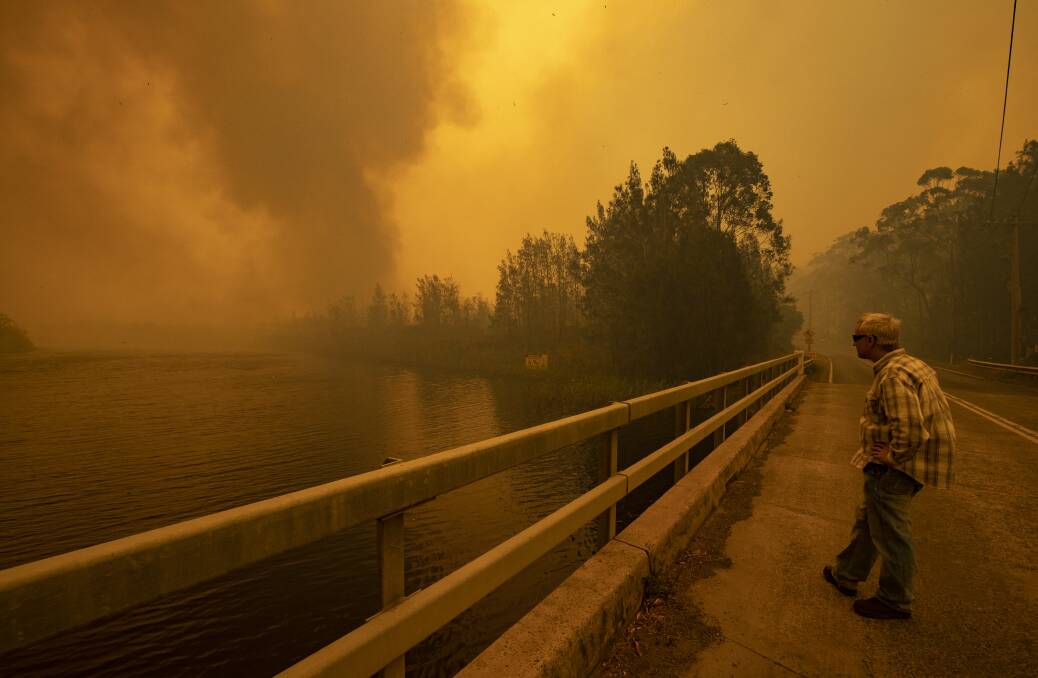 Jon Cleary watches a fire jump Willinga Lake as it approaches his property in Bawley Point. Picture: Sitthixay Ditthavong