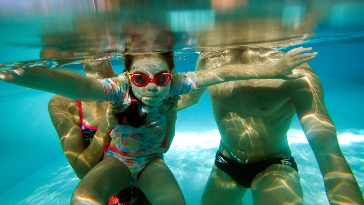 Underwater world: Chloe Saxby swims with Emma and David McKeon on Thursday. The McKeons' swim school held a pool party fundraiser for Chloe at Unanderra. Pictures: Sylvia Liber