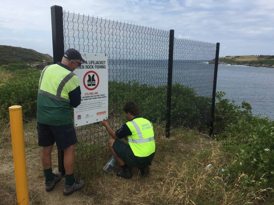 DANGER ZONE: Randwick City Council workers putting up a multi-lingual sign directing fisher to wear a lifejacket. Picture courtesy Randwick CC.