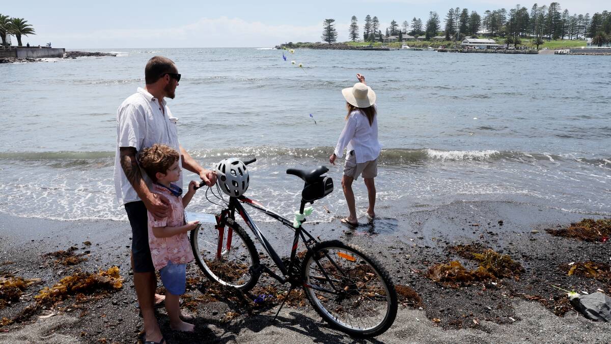 Tina Olsen throws a flower into the water in memory of her brother Allan as her son Peter Olsen Treloar and grandson Khorey watch on, standing beside Allan's bike. Picture by Sylvia Liber