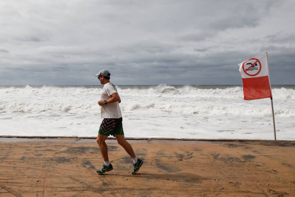 A runner passes along a wild Thirroul Beach on Saturday morning. Picture: Anna Warr