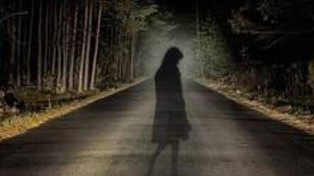 An image of a ghostly girl crossing a road in a dark forest. 