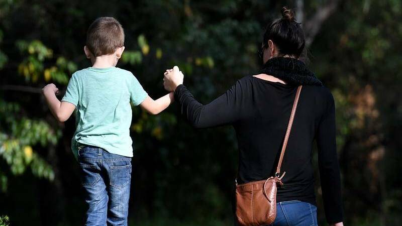 A mother holds her son's hand as he walks along a front garden wall. 