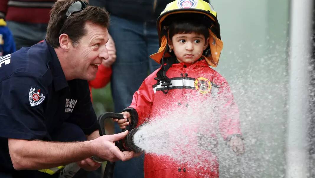 A fire fighter holds a hose while a child looks on. 