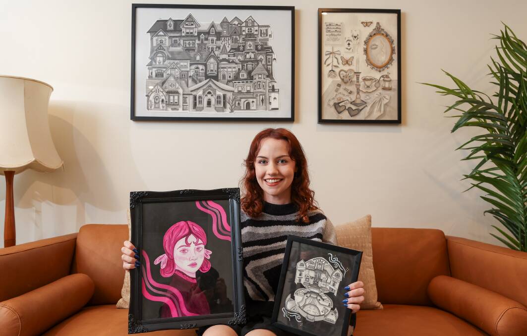 Artist Chloe Jean holding two of her pantings, with more on the wall behind her. Picture by Adam McLean