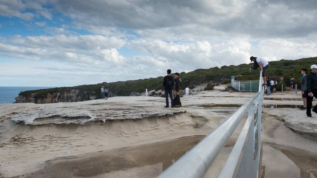 Tourists jump over safety barriers to take pictures on the fragile edge of Wedding Cake Rock. Photo: Mark Jesser