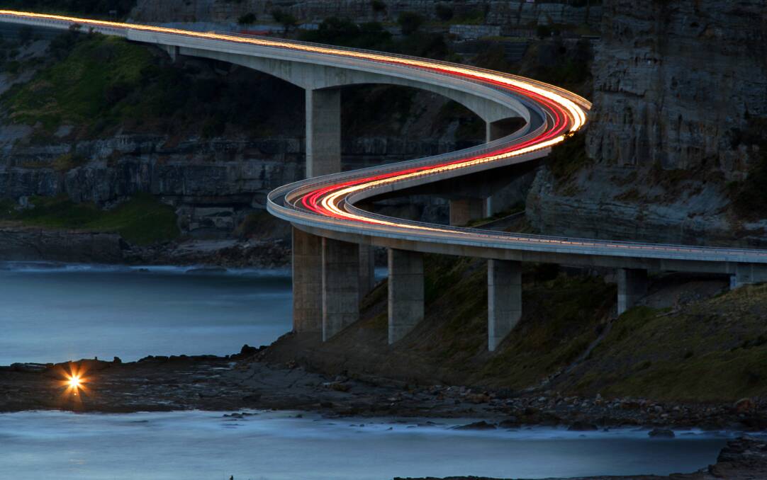 Sea Cliff Bridge seen at dusk, as car head and tail lights form a colourful trail during a lengthy exposure. Picture: ACM