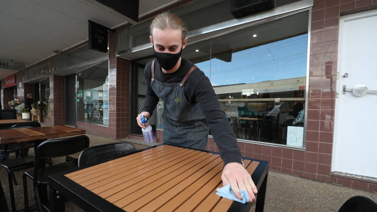 A masked Lochie Endicott wipes down a table at the Broken Drum Cafe in Fairy Meadow on Thursday. Picture: Robert Peet.