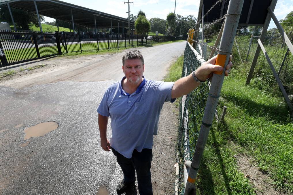 Glen Steggles at the gate to his business, which he has been told is too far from the node for an NBN connection. Behind him is the tip, which he has been told has an NBN connection. Photo: Robert Peet.