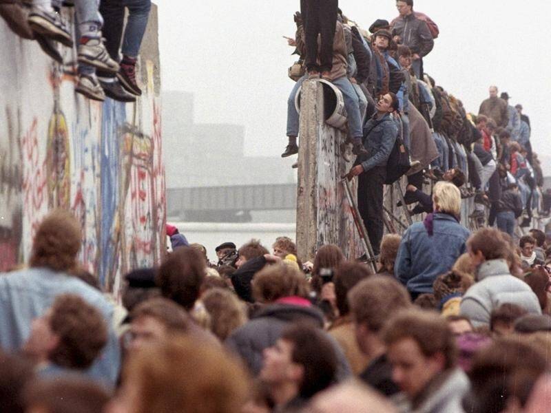 Berliners celebrate on top of the Berlin Wall as East Germans flood through the dismantled barrier.