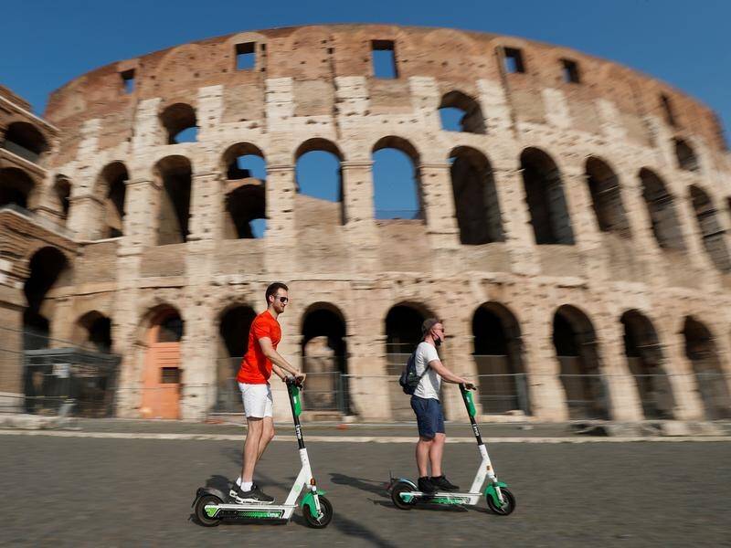 People ride electric scooters past the Colosseum in Rome.