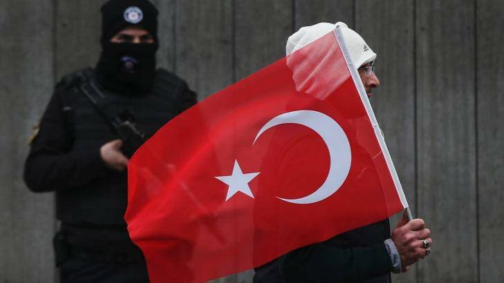A man with a Turkish flag walks past a police officer during a memorial outside the Reina club. The killer remains at large four days after the attack. Photo: Emrah Gurel