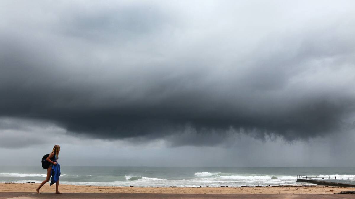 A girl walks along Austinmer Beach as storm clouds come over. Picture: KIRK GILMOUR