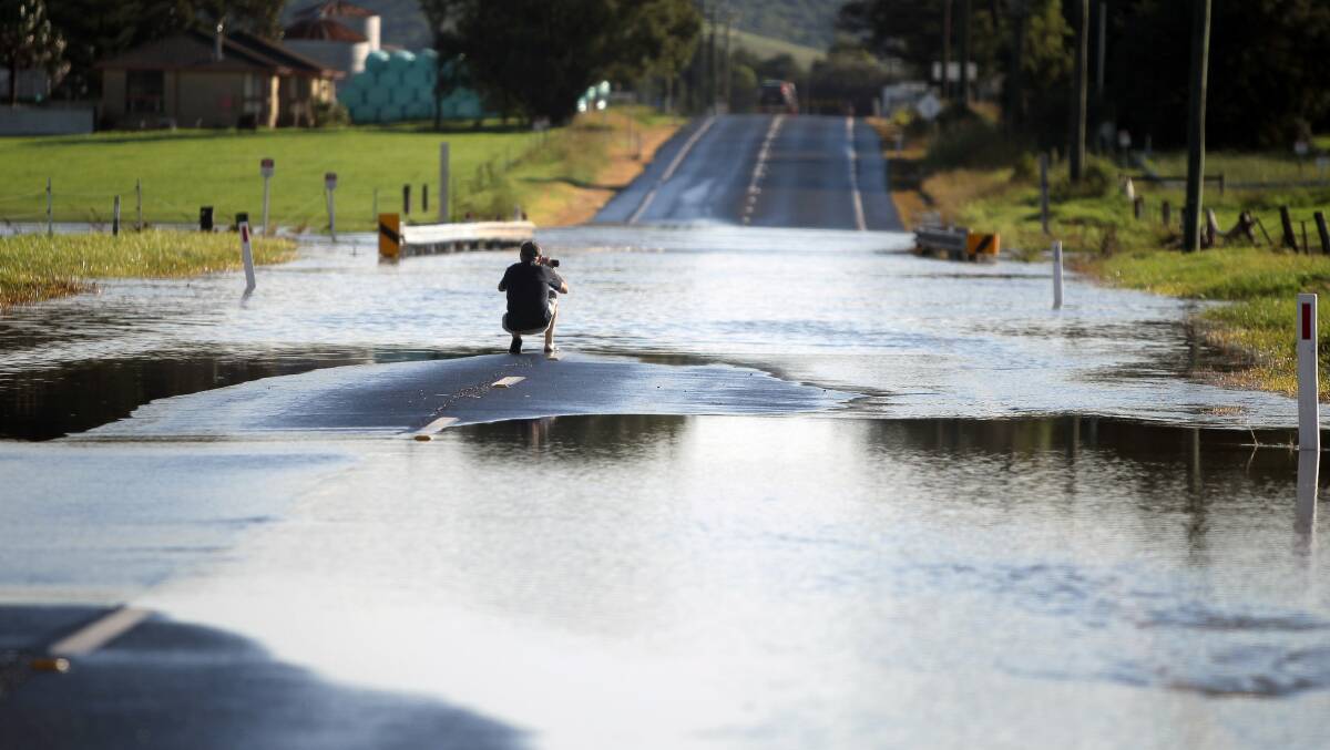 A man takes a photo of the flooded Illawarra Highway at Albion Park. Picture: SYLVIA LIBER