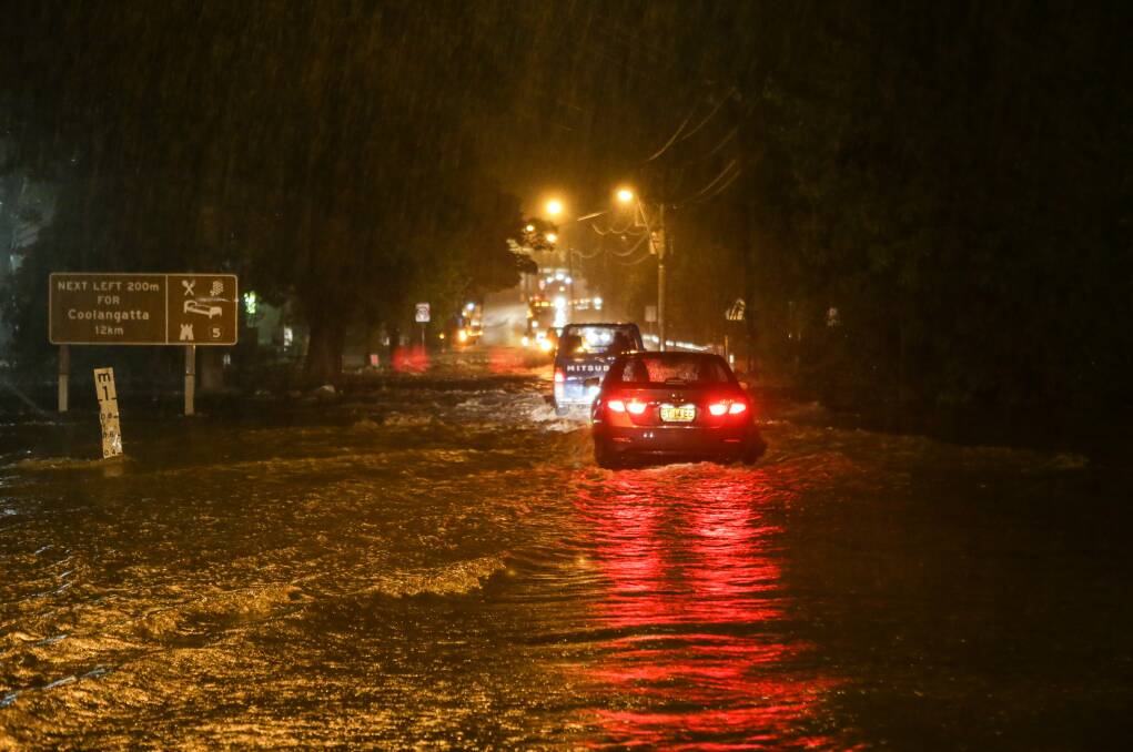 Cars crossing floodwaters across the Princes Highway in Berry. Picture: CHRISTOPHER CHAN
