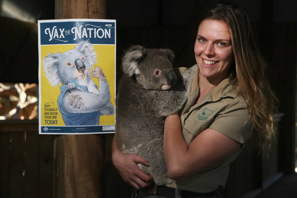 Free vaccination poster: Native zookeeper Elizabeth Florance with Johnny the koala in front of a Vax The Nation poster at Symbio Wildlife Park. Picture: Sylvia Liber.
