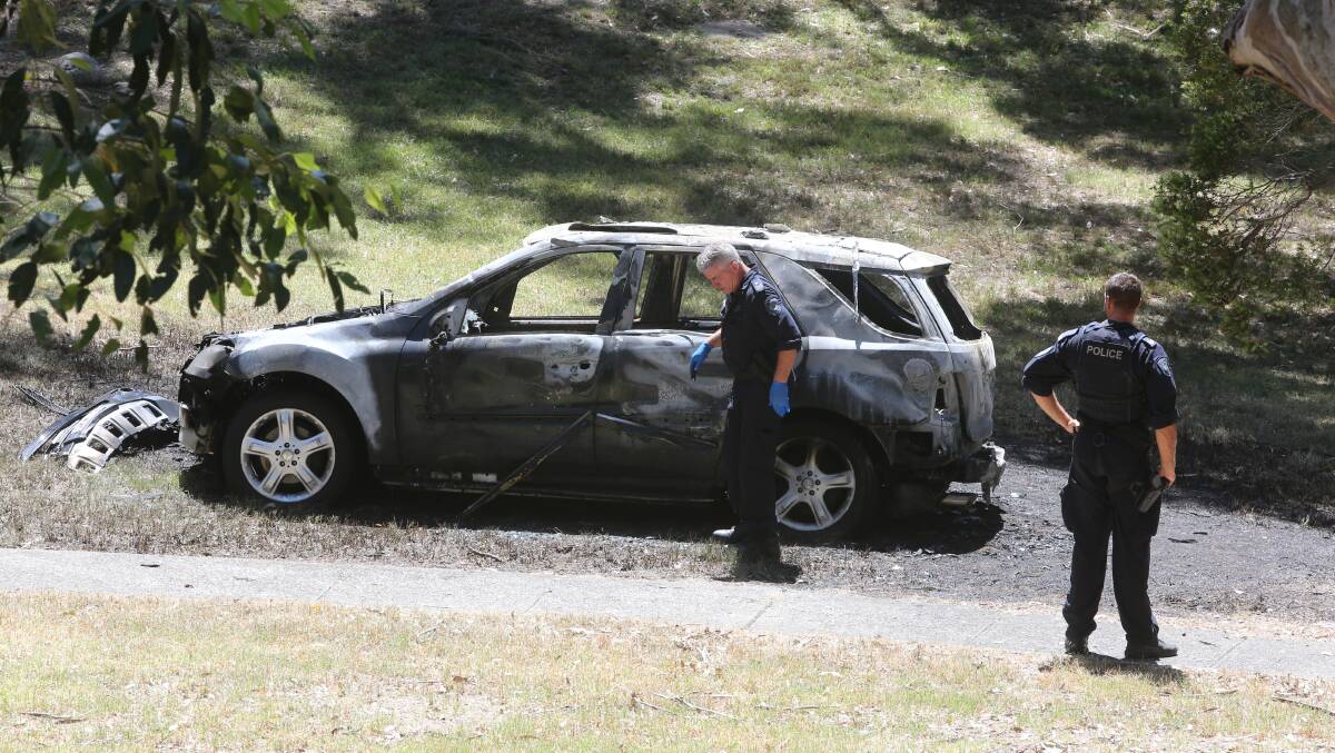 Police inspect the burnt-out car in a reserve off Derribong Drive at Cordeaux Heights. Police say it's unclear whether it is linked to the Unanderra shooting. Picture: Robert Peet