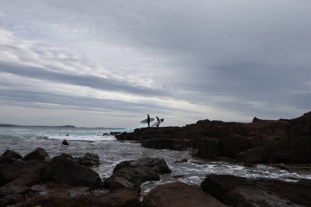 Surfers at a gloomy-looking Shellharbour beach. Picture: Sylvia Liber