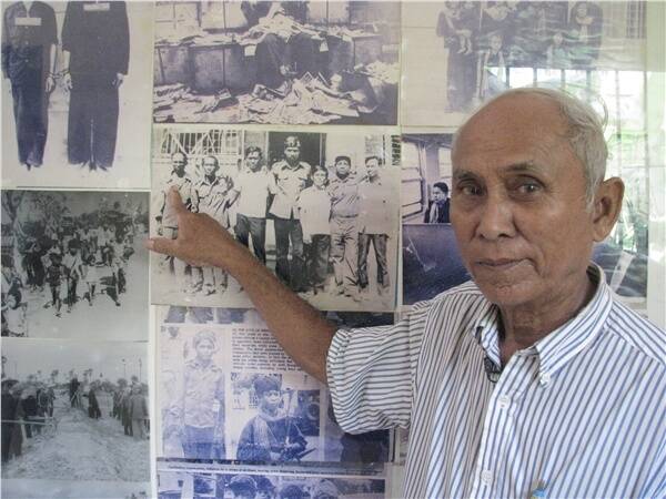 One of only three remaining survivors of S21 pointing at a photo of himself taken with the other survivors shortly after the fall of the Khmer Rouge.