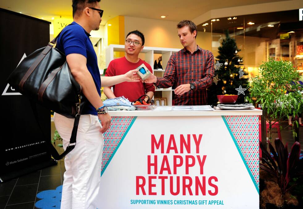 Tim Heng hands a keep cup to Sam Koh and David Goode at the Many Happy Returns desk at the shot tower in Melbourne Central. Photo: PENNY STEPHENS