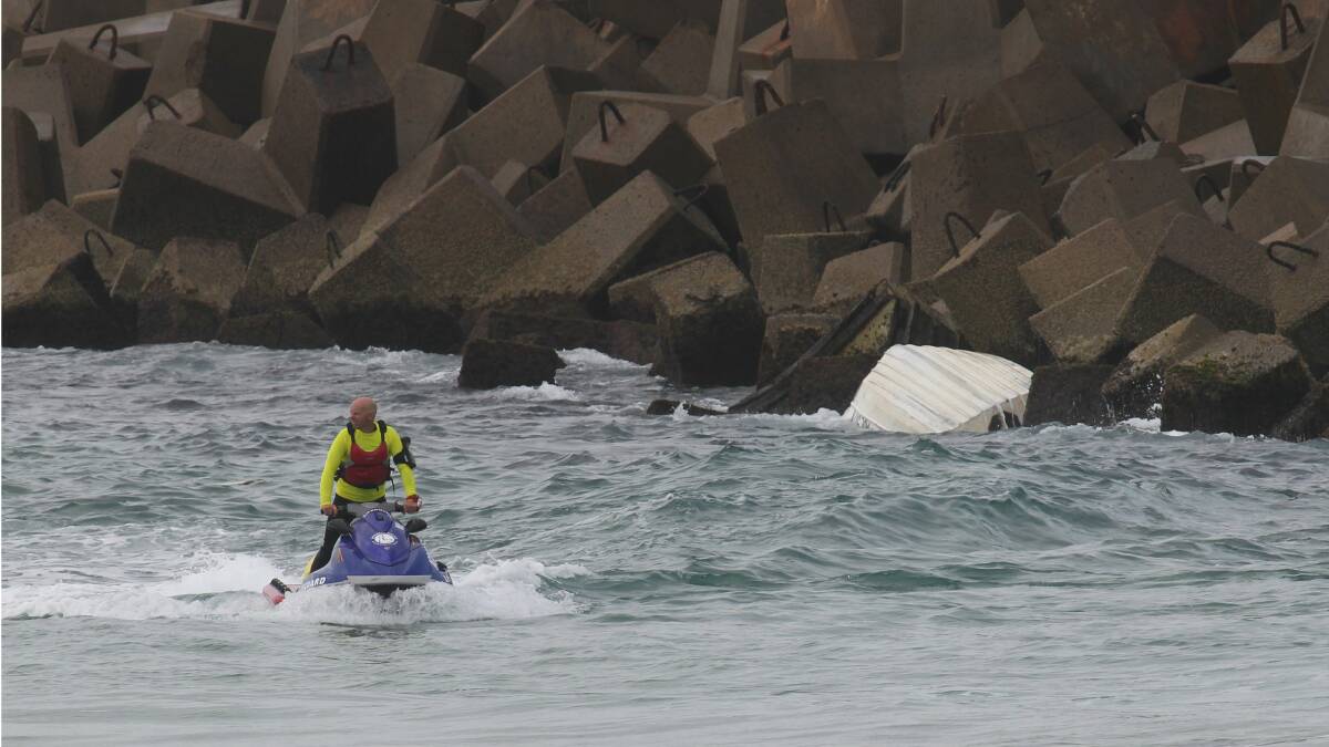 A Lifeguard searches water surrounding an overturned boat found wedged against the breakwall of the Port Kembla Coal Loader this morning. Picture: KEN ROBERTSON