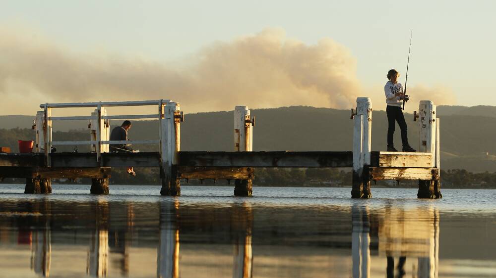 Fishermen at Boonerah Point yesterday afternoon against a backdrop of smoke from a bushfire at Robertson. Picture: DAVE TEASE