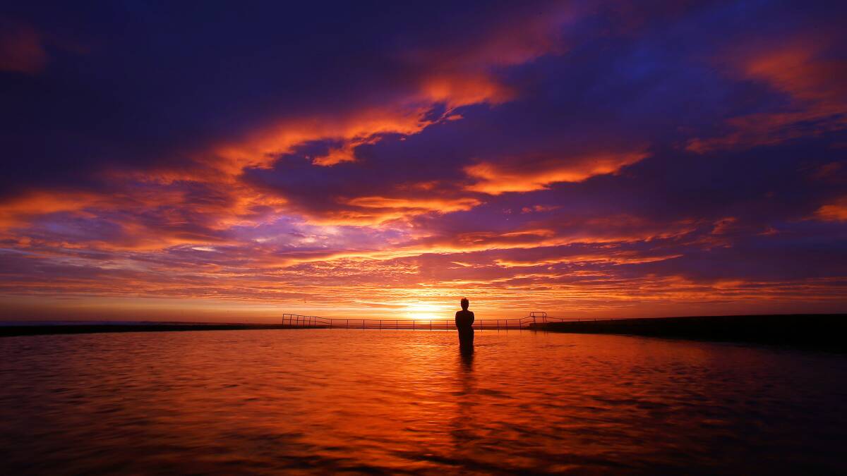 An early-morning swimmer watches the sunrise from Austinmer pool. Pictures: KIRK GILMOUR