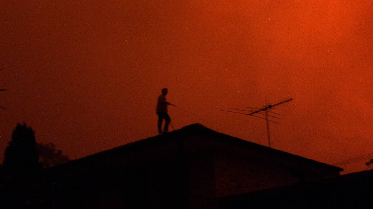 A Canberra man hoses down his roof ahead of bushfires in 2001. Picture: JACKY GHOSSEIN 