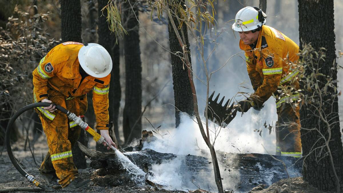 Firefighters douse burning logs from the Wandanadian fire. Picture: AFP