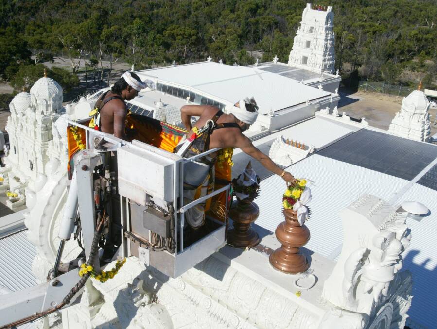 Riding on the platform of a cherry picker, Hindu priests pour holy water to consecrate the new 30m towers of the Sri Venkateswara Temple at Helensburgh.