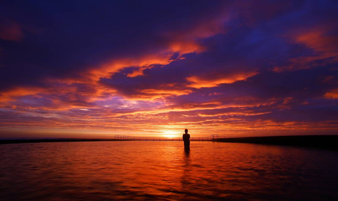 A swimmer watches the sun rise from Austinmer pool on the last day of summer. Picture: KIRK GILMOUR